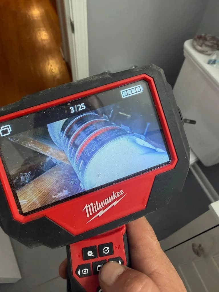 Handheld sewer inspection camera monitor displaying a live video feed from inside a drain pipe