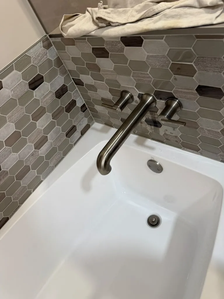 New brushed nickel tub filler faucet installed above a white tub with mosaic tile surround