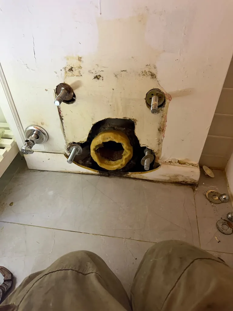 Toilet flange and supply valve exposed on a bathroom floor with a water-damaged wall behind it