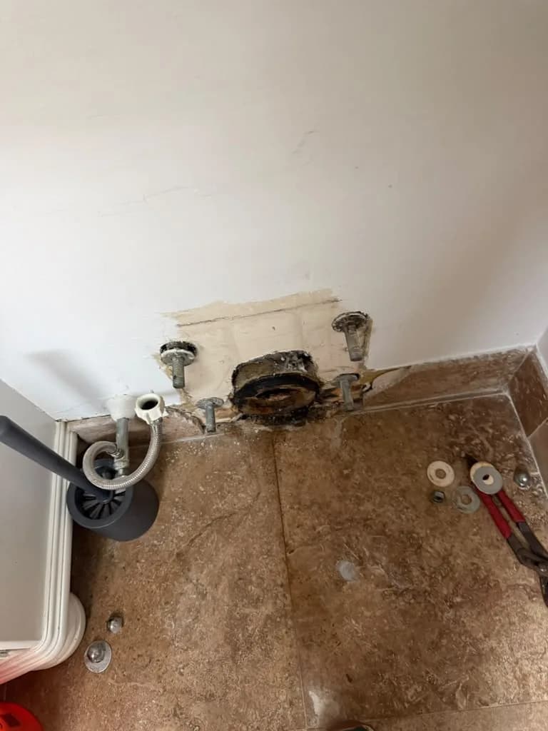 Toilet floor flange bolts exposed on tile flooring with pliers and hardware nearby