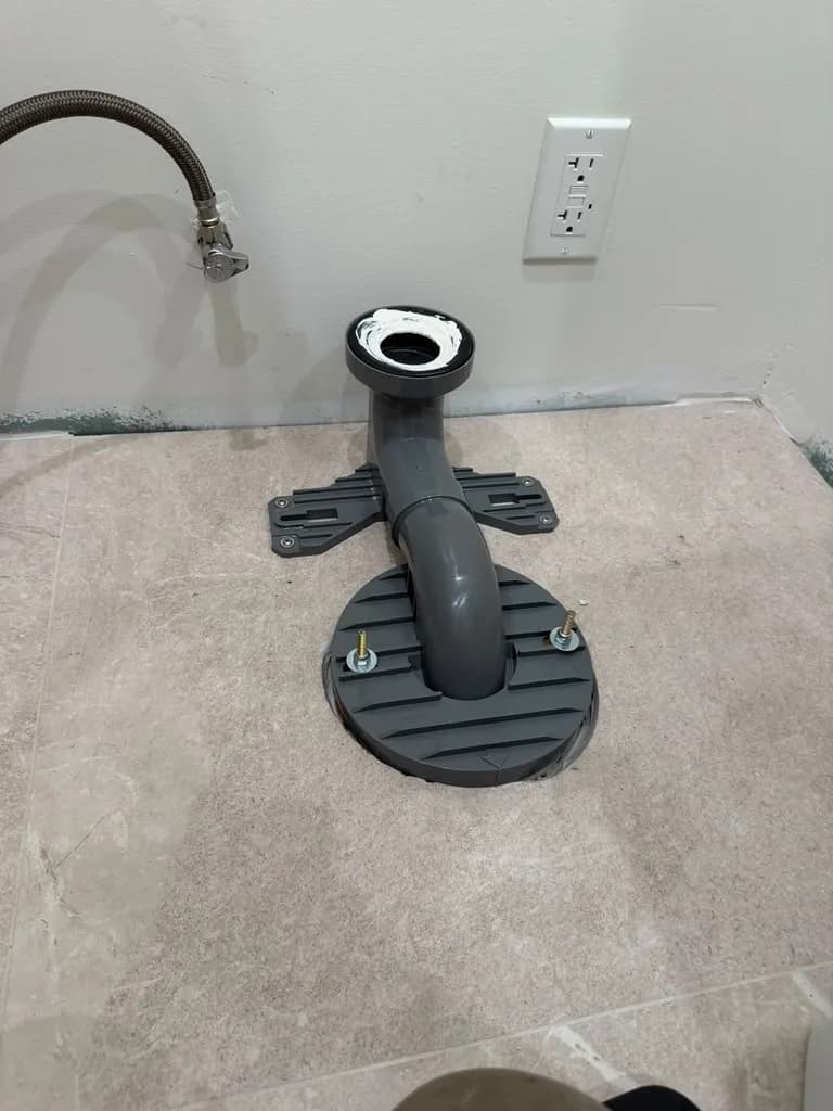 New toilet flange installed in a bathroom floor next to an electrical outlet