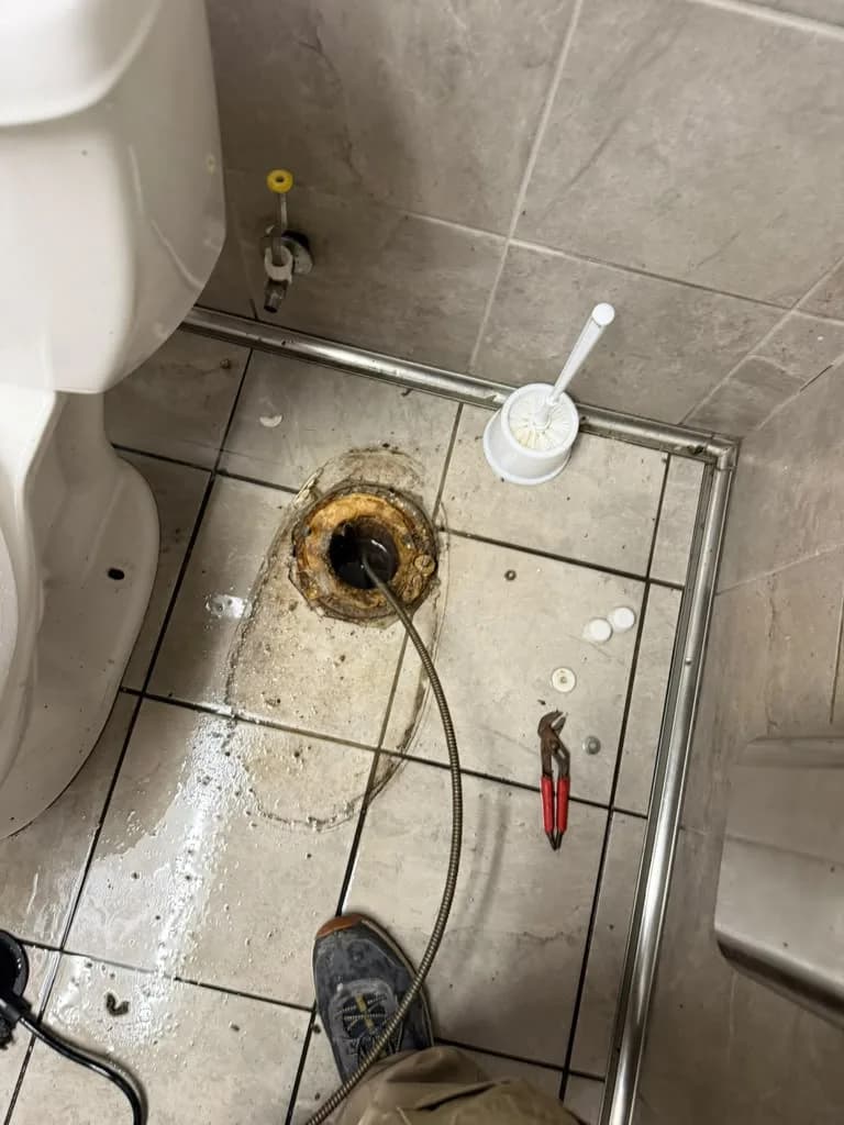 Old corroded toilet flange being removed with a wrench