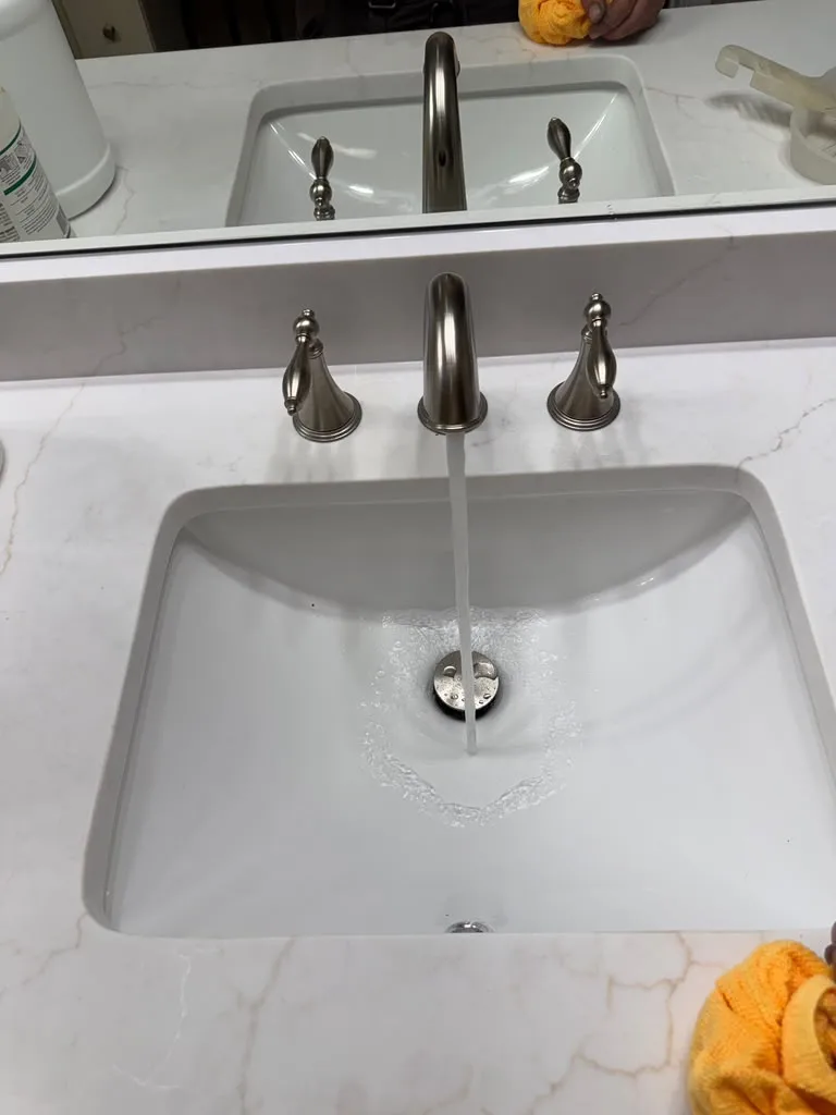 Water running from a newly installed brushed nickel bathroom faucet into a white sink