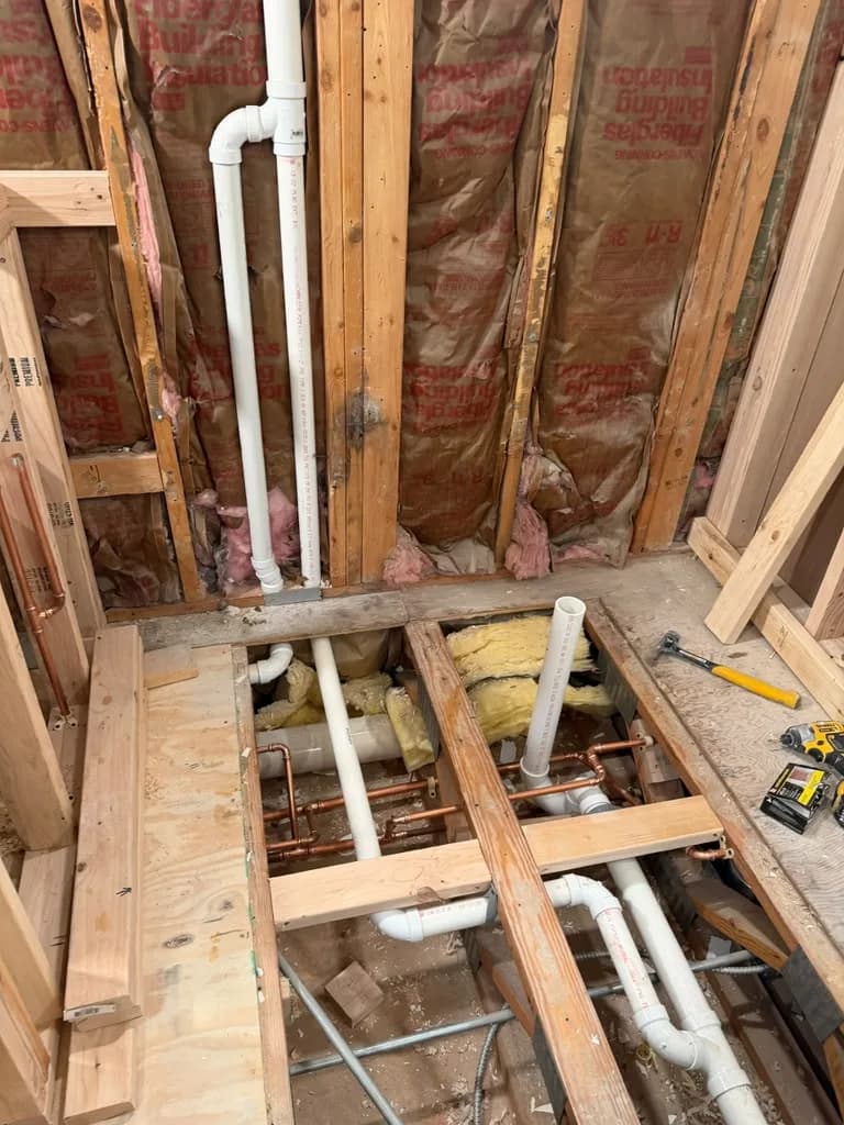 New copper and PVC drain pipes running through a floor and ceiling cavity during a bathroom rough-in