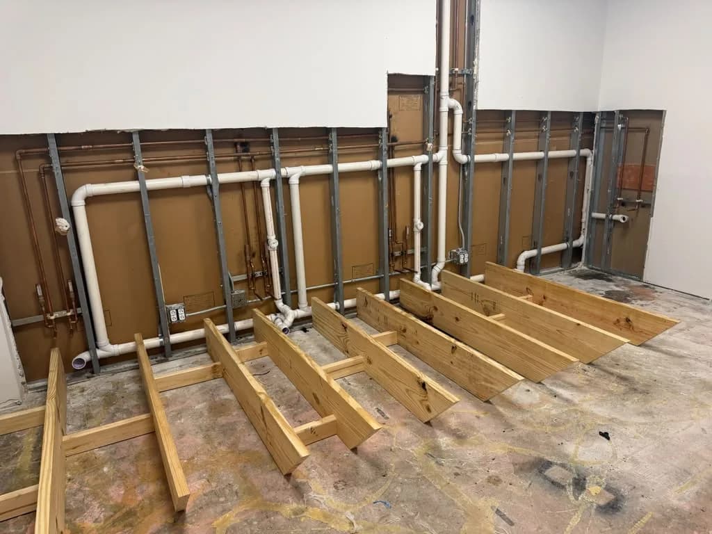 Wide view of copper and PVC supply and drain pipes stubbed out along a framed wall