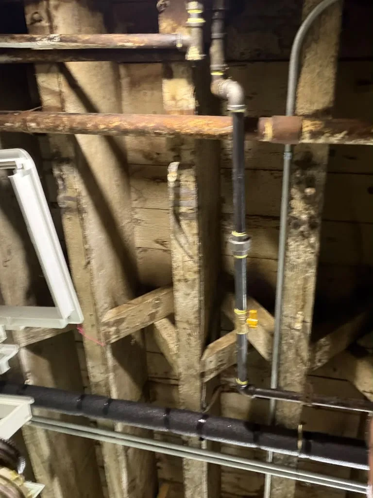 Old galvanized and black iron pipe running through wood ceiling joists