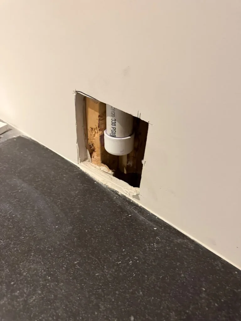 Access hole cut into drywall exposing a PVC pipe stub-out