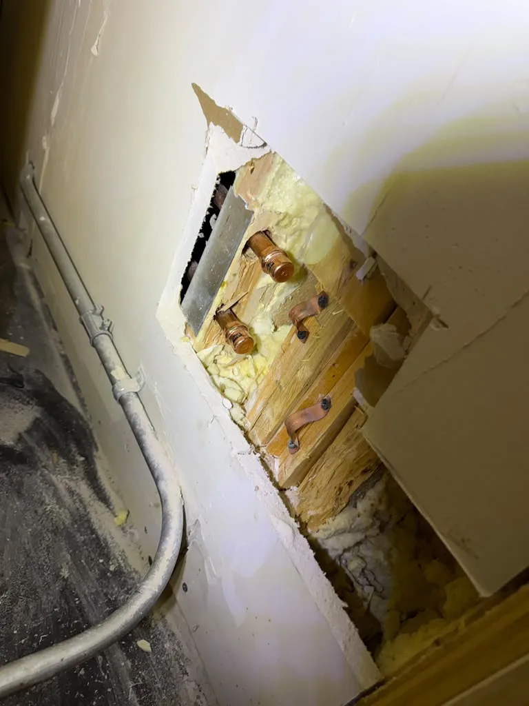 Access hole cut into drywall exposing copper pipe stub-outs with insulation